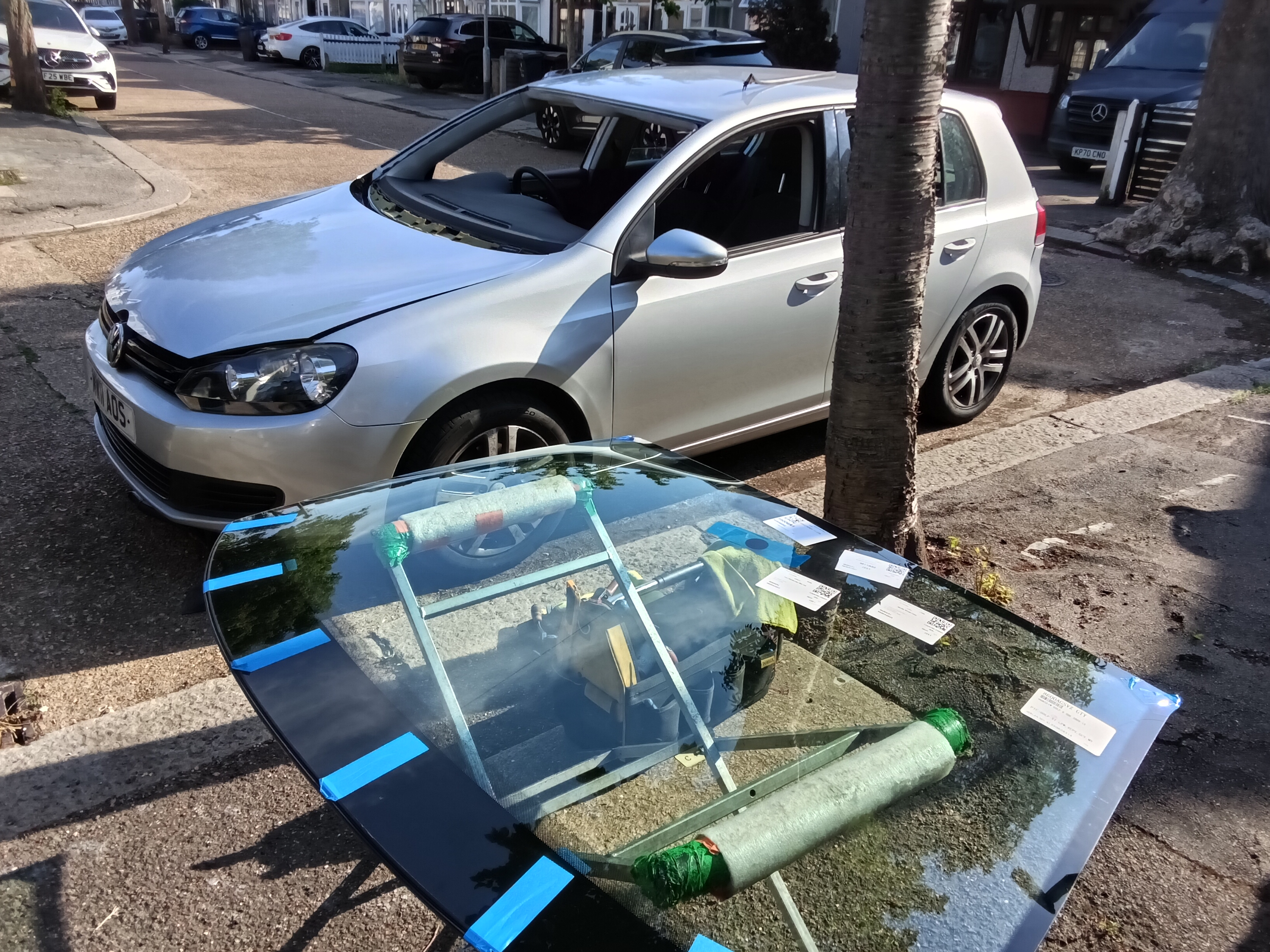 JJ Windscreens mobile technician with new VW Golf windscreen ready for fitting on a residential street